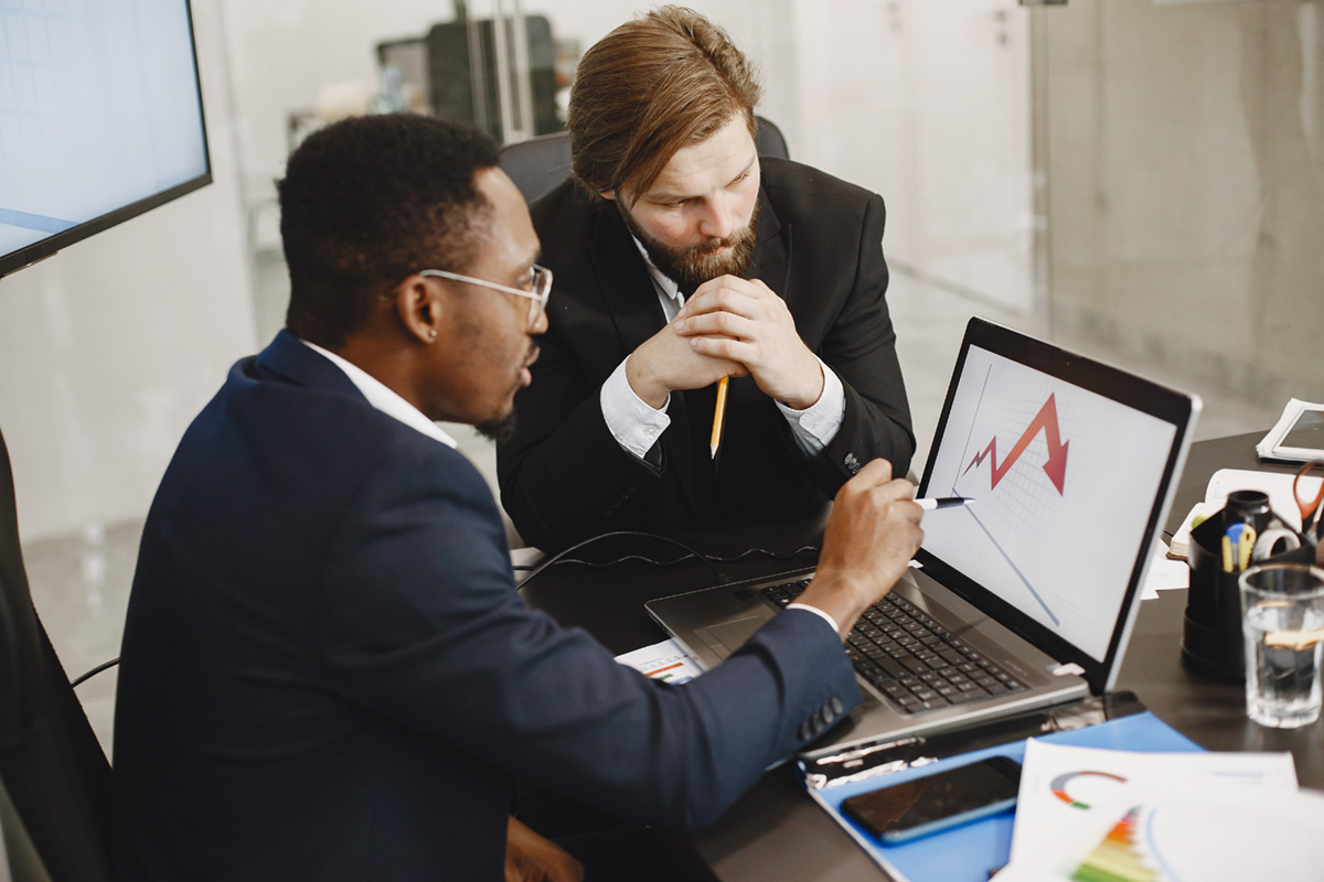 Two males in business suit reviewing a chart on a computer.