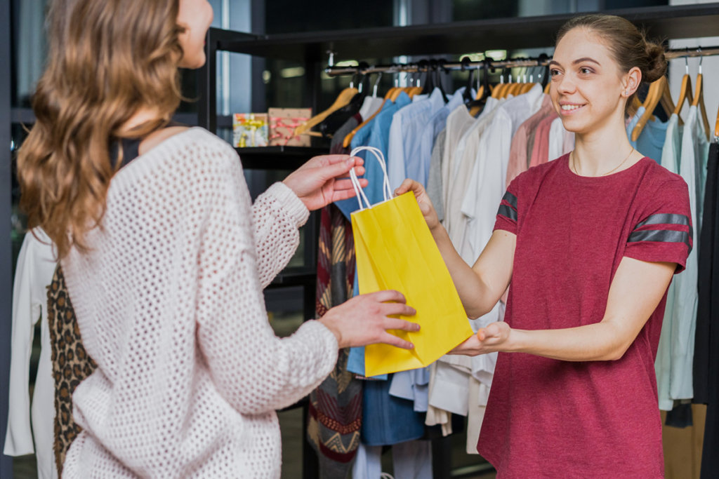 A female retailer handing a shopping bag to a customer.